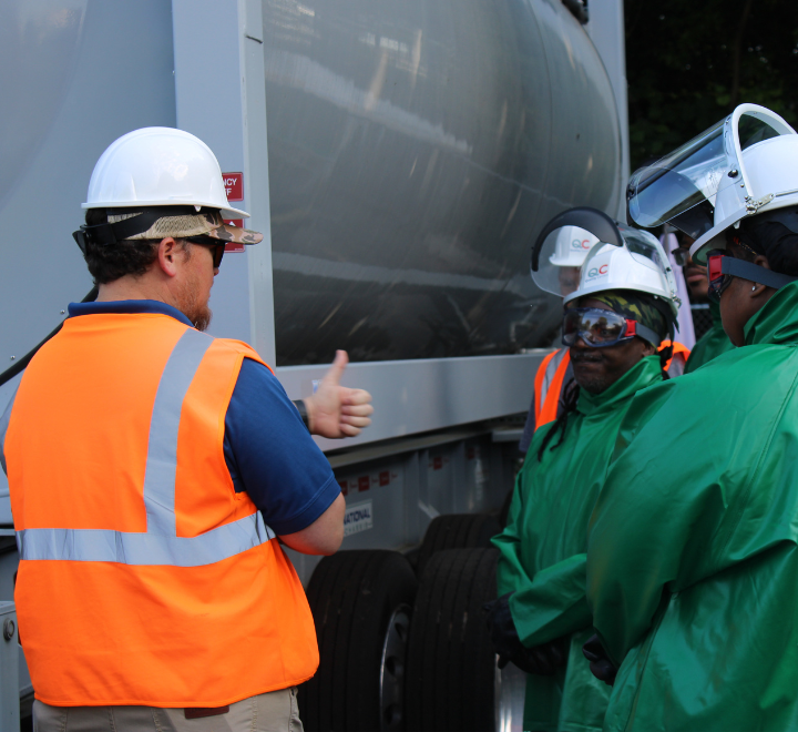 QC Inc team members in safety gear meeting beside a tanker trailer.